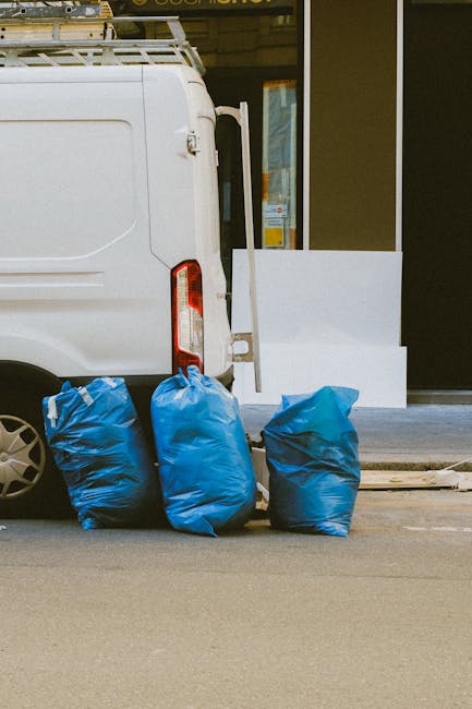 The image depicts the rear section of a white commercial van parked on a city street, with three large blue rubbish bags placed neatly on the pavement beside the vehicle. The rubbish bags are made of 